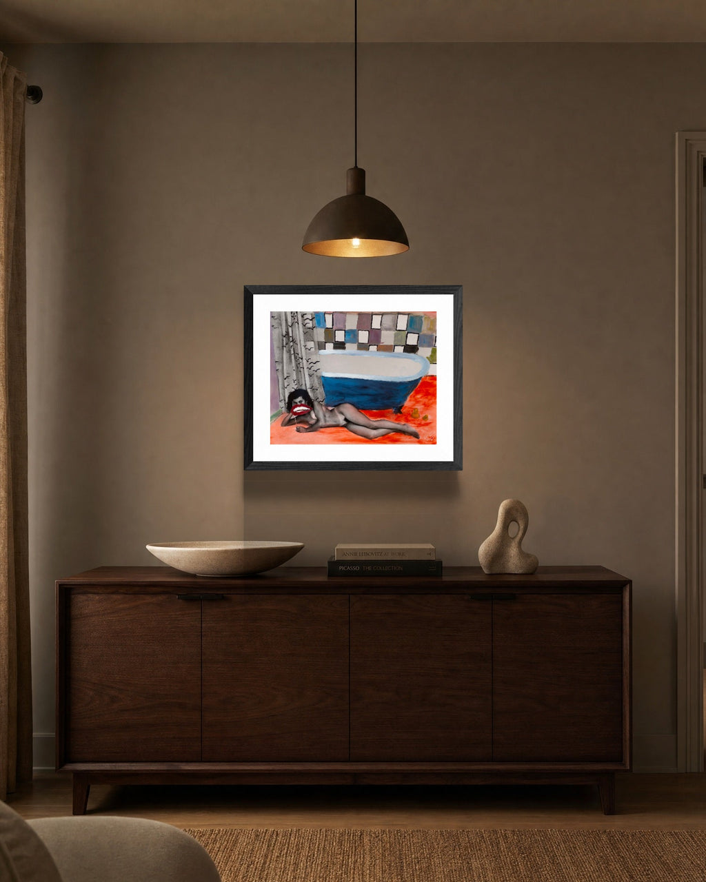 Framed artwork on a wall above a wooden cabinet in a room.